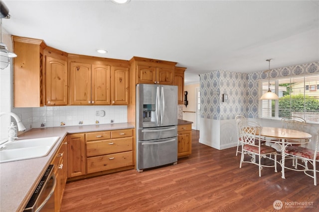 kitchen with appliances with stainless steel finishes, a sink, wallpapered walls, wood finished floors, and decorative light fixtures