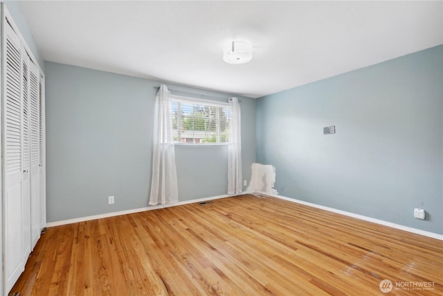 unfurnished bedroom featuring wood finished floors, baseboards, and a closet