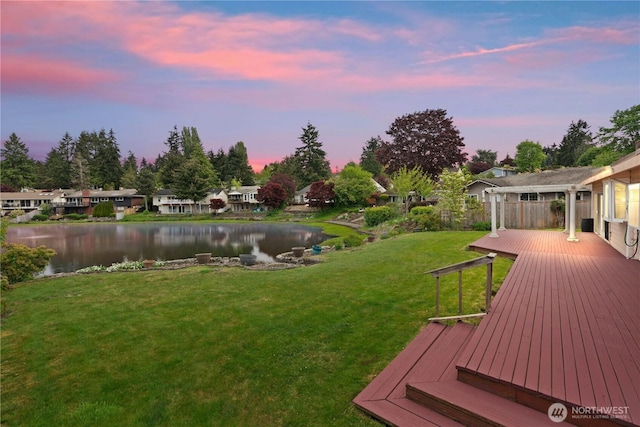 view of grassy yard featuring a deck with water view