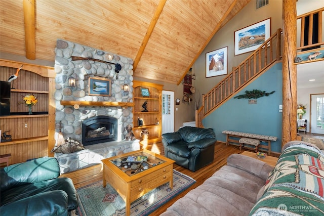 living room featuring wooden ceiling, wood finished floors, stairs, a stone fireplace, and high vaulted ceiling