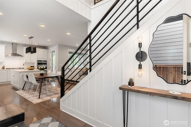 stairway with wood finished floors, recessed lighting, and a decorative wall