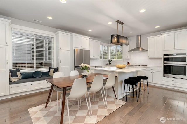 kitchen featuring wall chimney range hood, appliances with stainless steel finishes, white cabinets, light wood finished floors, and recessed lighting