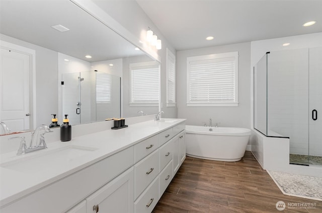 bathroom with a stall shower, wood finished floors, a soaking tub, recessed lighting, and double vanity
