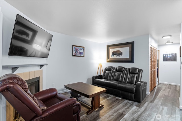 living area with a tile fireplace, wood finished floors, and baseboards
