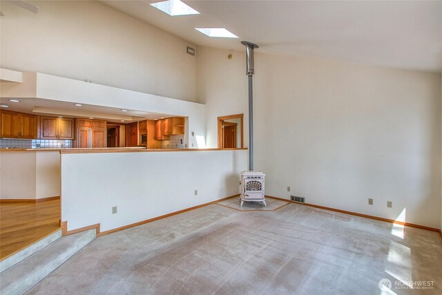55 Langell Ln, Orcas Island, WA 98245 - unfurnished living room with a wood stove, a skylight, high vaulted ceiling, baseboards, and light colored carpet