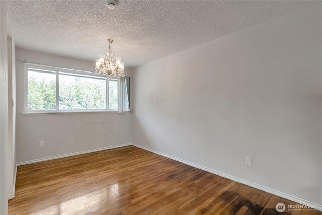 14502 Main St, Bellevue, WA 98007 - empty room with a chandelier, hardwood / wood-style floors, baseboards, and a textured ceiling