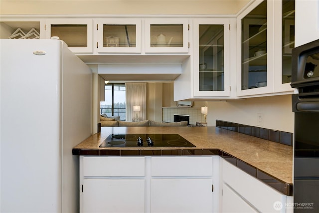 kitchen featuring black electric stovetop, freestanding refrigerator, white cabinets, glass insert cabinets, and dark countertops