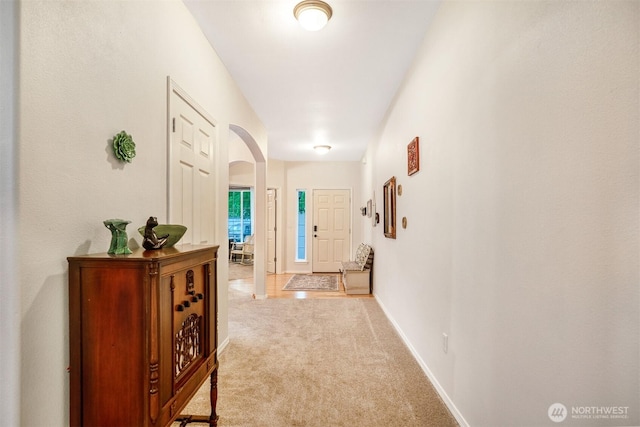 hallway with carpet flooring, arched walkways, and baseboards