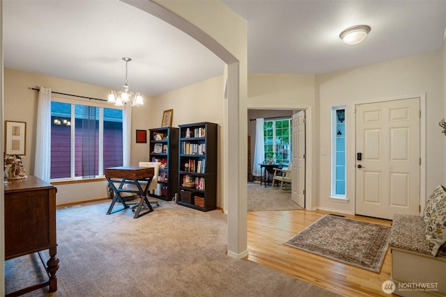 carpeted entryway featuring arched walkways, a chandelier, and baseboards