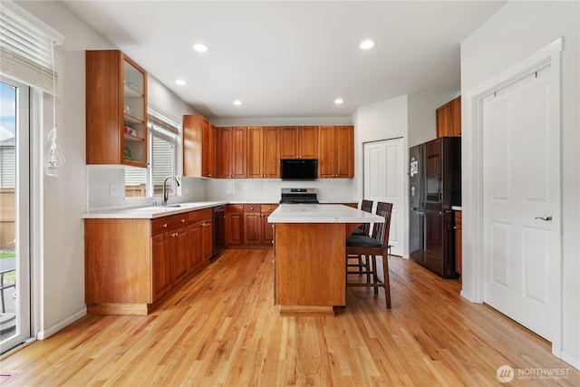 kitchen with black appliances, healthy amount of natural light, a kitchen breakfast bar, brown cabinets, and recessed lighting