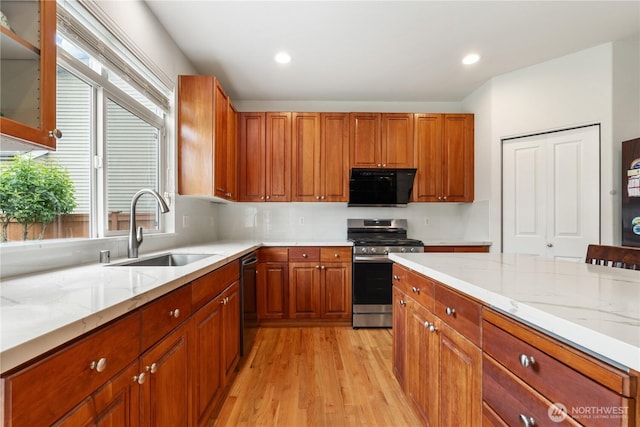 kitchen featuring stainless steel gas range oven, a sink, light wood-style floors, dishwashing machine, and light stone counters