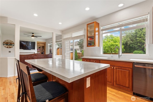 kitchen featuring dishwasher, a sink, light stone countertops, a breakfast bar area, and recessed lighting