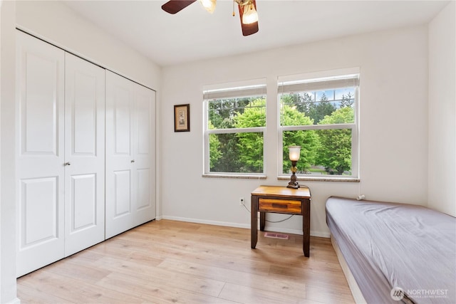bedroom featuring multiple windows, light wood finished floors, baseboards, and a closet
