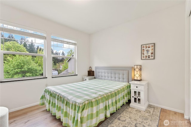 bedroom featuring baseboards, light wood finished floors, and multiple windows