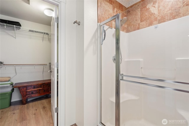 full bath with a stall shower, a spacious closet, and wood finished floors