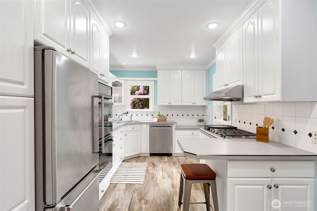 kitchen with appliances with stainless steel finishes, under cabinet range hood, a peninsula, white cabinetry, and recessed lighting