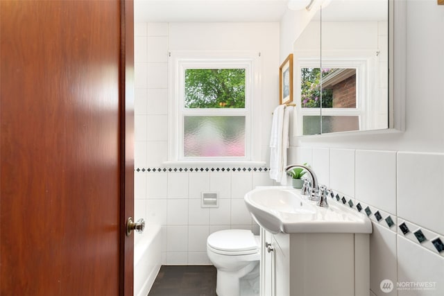 full bathroom with tile walls, toilet, vanity, and a bathtub