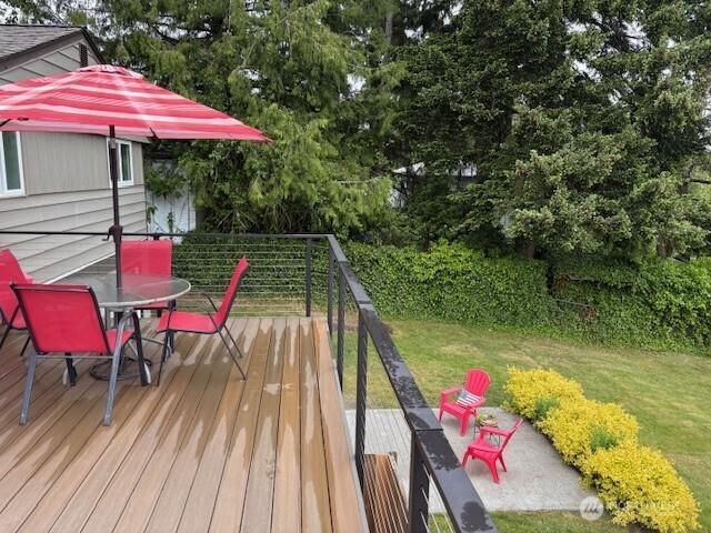 10644 19th Ave SW, Seattle, WA 98146 - deck with outdoor dining area, a lawn, and view of wooded area