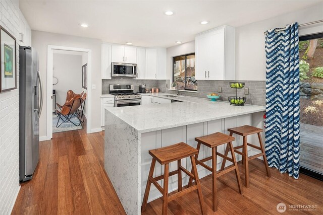 6700 81st Ave SE, Mercer Island, WA 98040 - kitchen with stainless steel appliances, a sink, wood finished floors, a peninsula, and light stone countertops