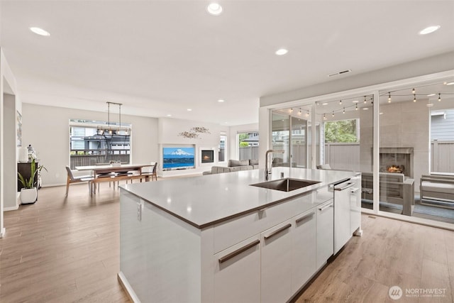 24821 237th Ln SE, Maple Valley, WA 98038 - kitchen featuring a sink, white cabinets, a kitchen island with sink, light wood finished floors, and a warm lit fireplace