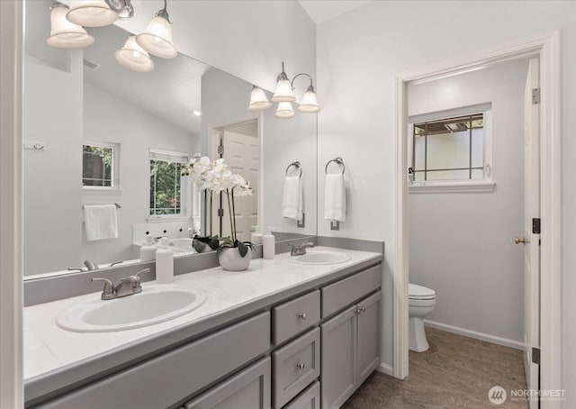 bathroom featuring toilet, double vanity, baseboards, lofted ceiling, and a bath