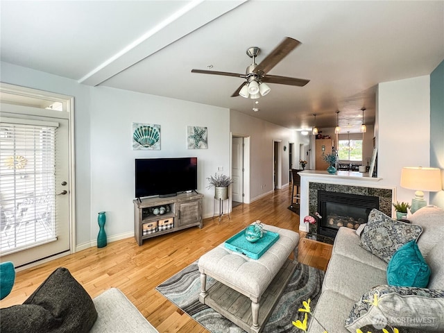 living room featuring a ceiling fan, a premium fireplace, wood finished floors, and baseboards