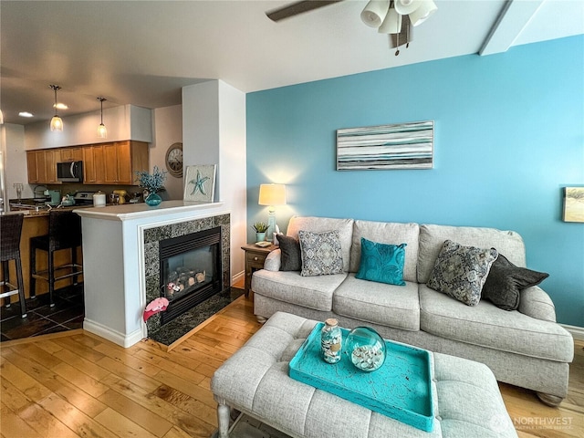 living room with light wood-style floors, a ceiling fan, baseboards, and a high end fireplace