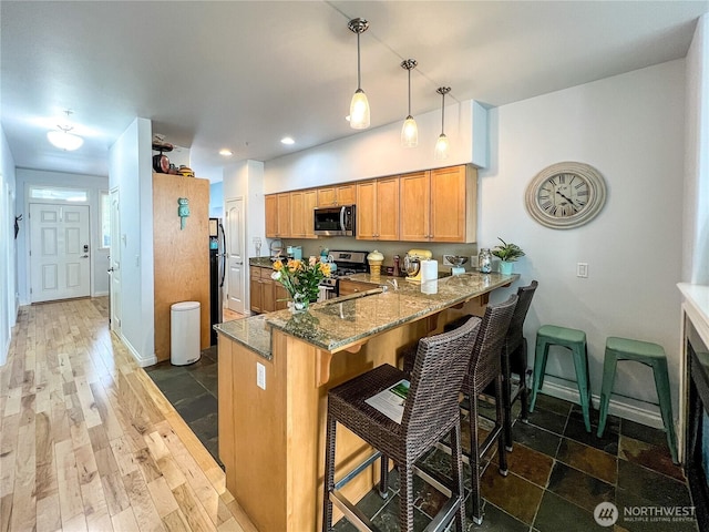 kitchen with appliances with stainless steel finishes, dark stone countertops, a peninsula, a breakfast bar area, and recessed lighting