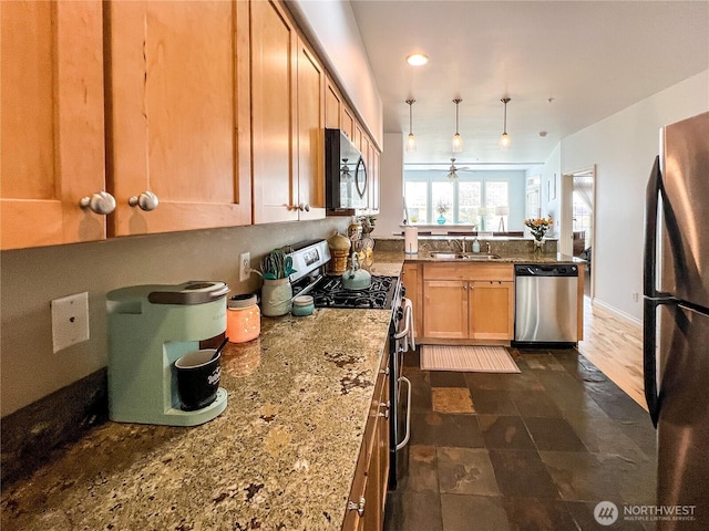 kitchen featuring stainless steel appliances, a sink, a peninsula, light stone countertops, and hanging light fixtures
