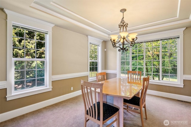 carpeted dining space featuring a chandelier, a tray ceiling, crown molding, and baseboards