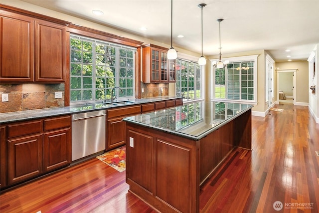 kitchen featuring dishwasher, wood finished floors, decorative backsplash, a sink, and hanging light fixtures