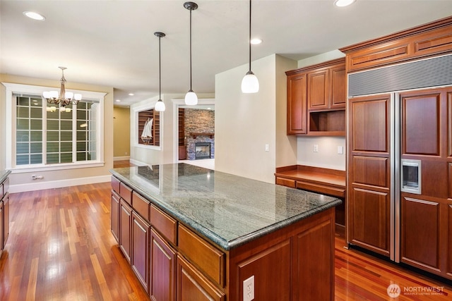 kitchen featuring paneled built in fridge, wood finished floors, a fireplace, a center island, and recessed lighting