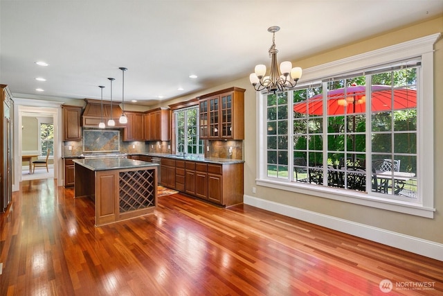 kitchen with a sink, brown cabinetry, a chandelier, a kitchen island, and dark wood-style flooring