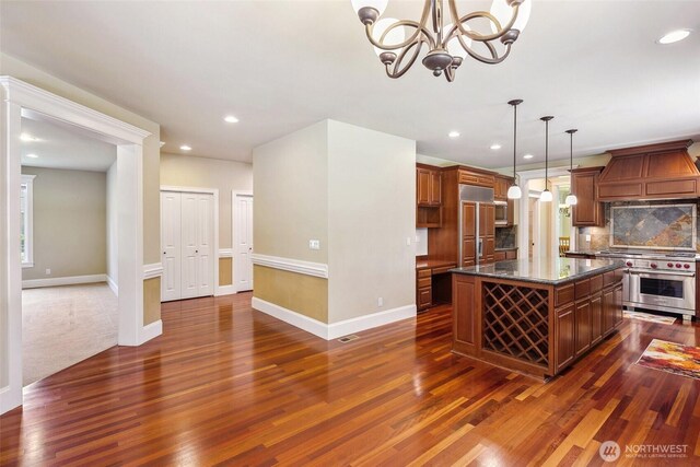 kitchen with high end appliances, dark wood-type flooring, custom range hood, baseboards, and backsplash