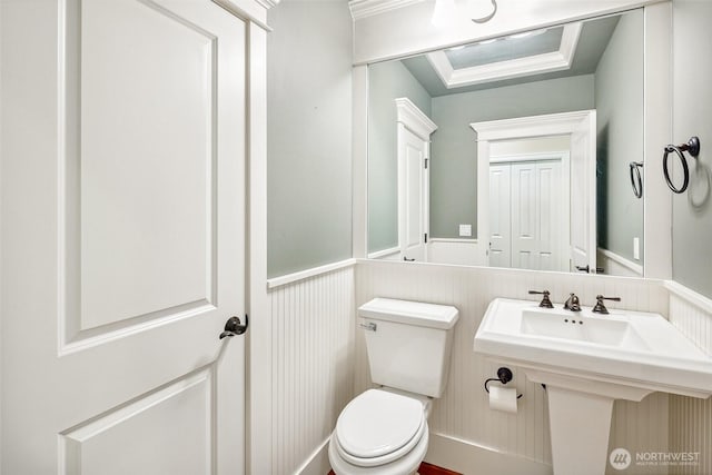 half bath with toilet, wainscoting, and a decorative wall