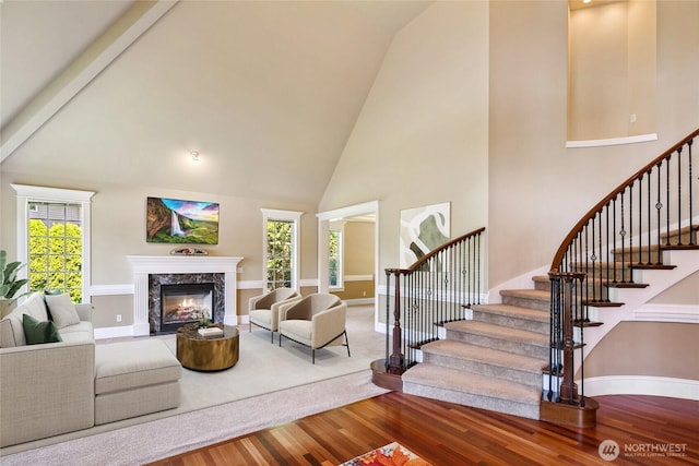 living room with wood finished floors, high vaulted ceiling, stairs, baseboards, and a fireplace