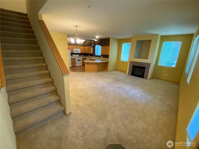 unfurnished living room with stairway, light colored carpet, a tiled fireplace, and a chandelier
