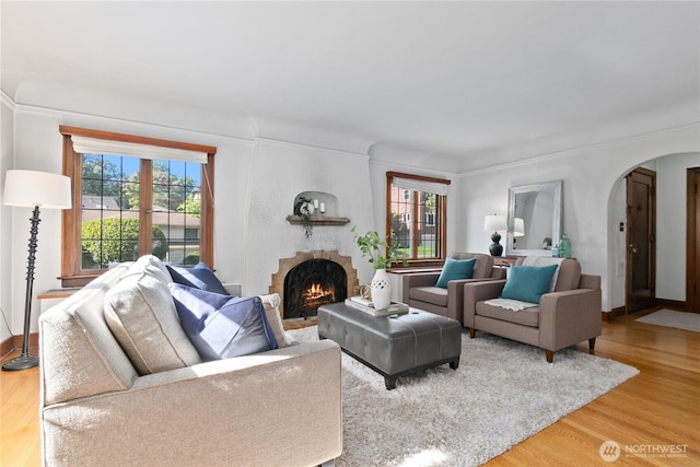 living room with arched walkways, plenty of natural light, a fireplace, and light wood-type flooring