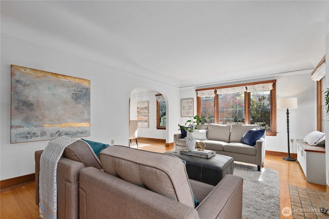 living area featuring arched walkways, baseboards, light wood-style flooring, and ornamental molding