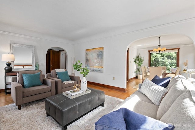 living area featuring arched walkways, a chandelier, wood finished floors, baseboards, and crown molding