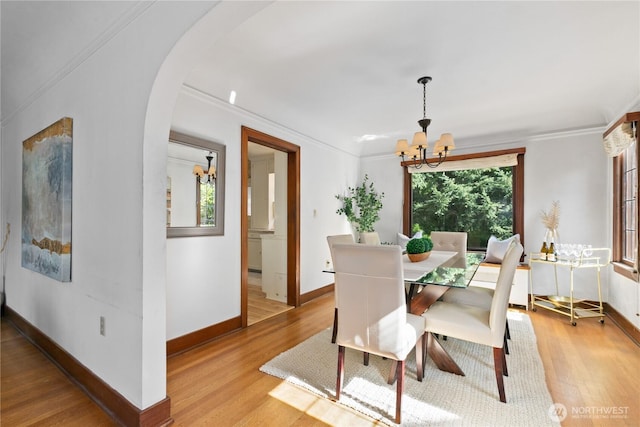 dining space featuring a chandelier, light wood-type flooring, arched walkways, baseboards, and crown molding