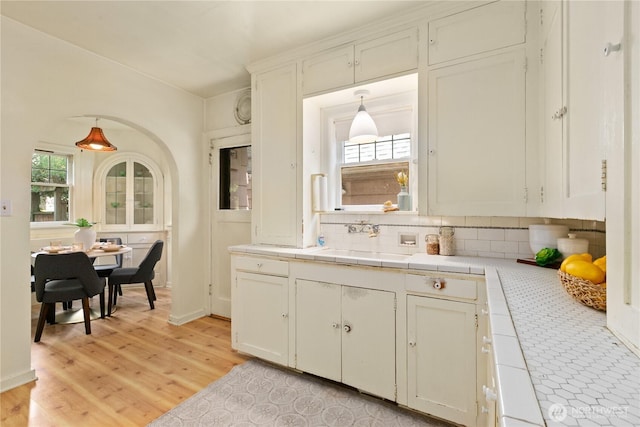 kitchen with tile countertops, a sink, decorative backsplash, and light wood finished floors