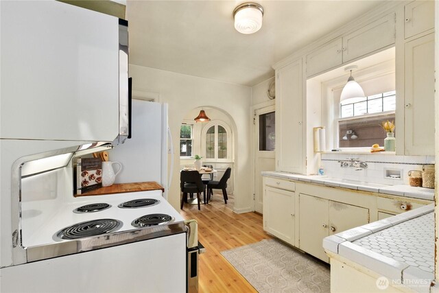 kitchen with white appliances, tile counters, a sink, light wood finished floors, and healthy amount of natural light