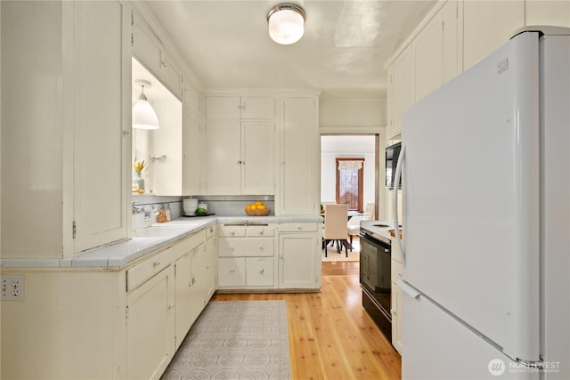 kitchen featuring freestanding refrigerator, range with electric cooktop, light countertops, light wood-type flooring, and decorative backsplash