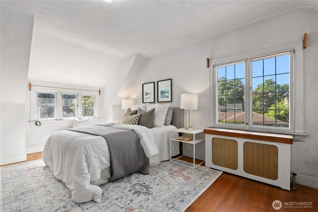 bedroom with wood finished floors, lofted ceiling, and radiator heating unit