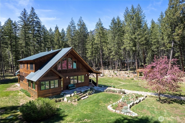 back of house with a wooded view, a lawn, and metal roof