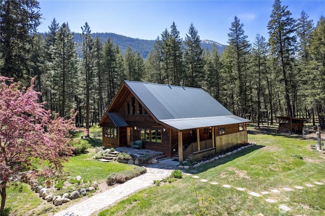 view of front of house with covered porch, a forest view, a front yard, metal roof, and a mountain view