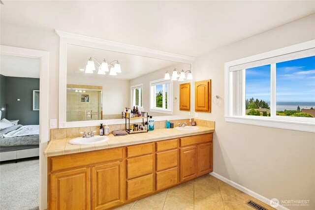 bathroom featuring a stall shower, double vanity, baseboards, tile patterned floors, and ensuite bathroom
