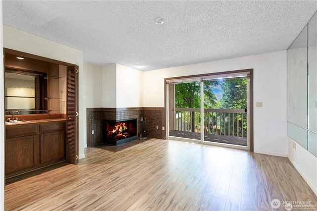 12840 SE 40th Ct Unit B2, Bellevue, WA 98006 - unfurnished living room featuring light wood-style floors, a brick fireplace, a textured ceiling, baseboards, and a sink