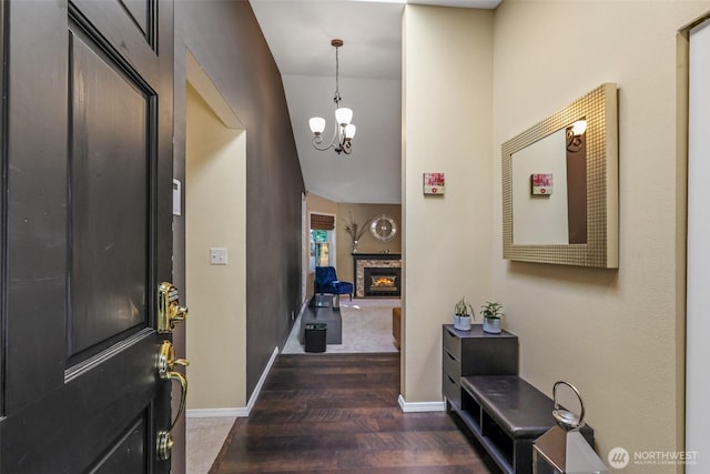 foyer entrance with dark wood-type flooring, a chandelier, baseboards, and a fireplace